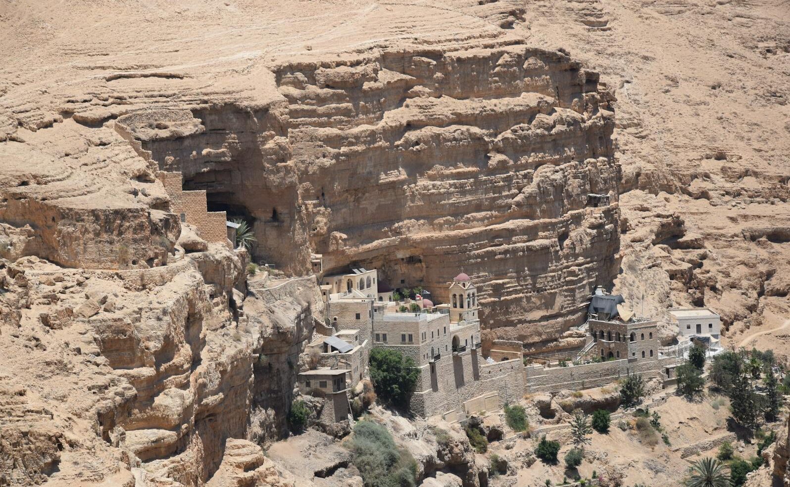 Aerial view of St George's Monastery nestled in the cliffs of Wadi Qelt, illuminated by bright sunlight.